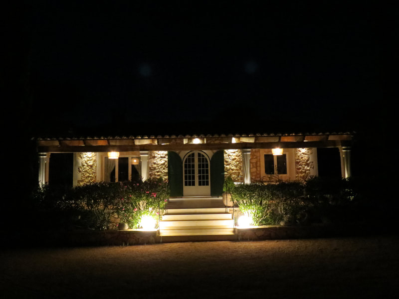The finca at night, its facade and pergola lit warm from below, the arched door glowing between the windows