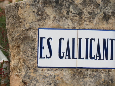 The house's own hand-painted blue-on-white ceramic tile sign reading ES GALLICANT, set into a weathered stone gatepost