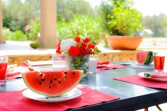 Close up of the breakfast table: a slice of watermelon on a white plate and a small posy of red and white roses